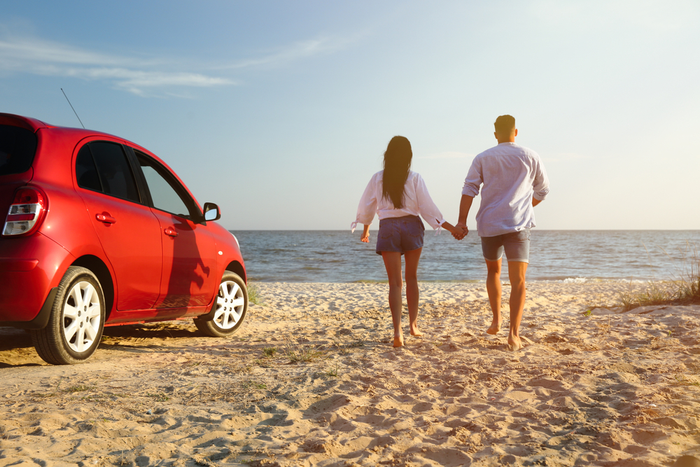 couple running on sandy beach by parked car
