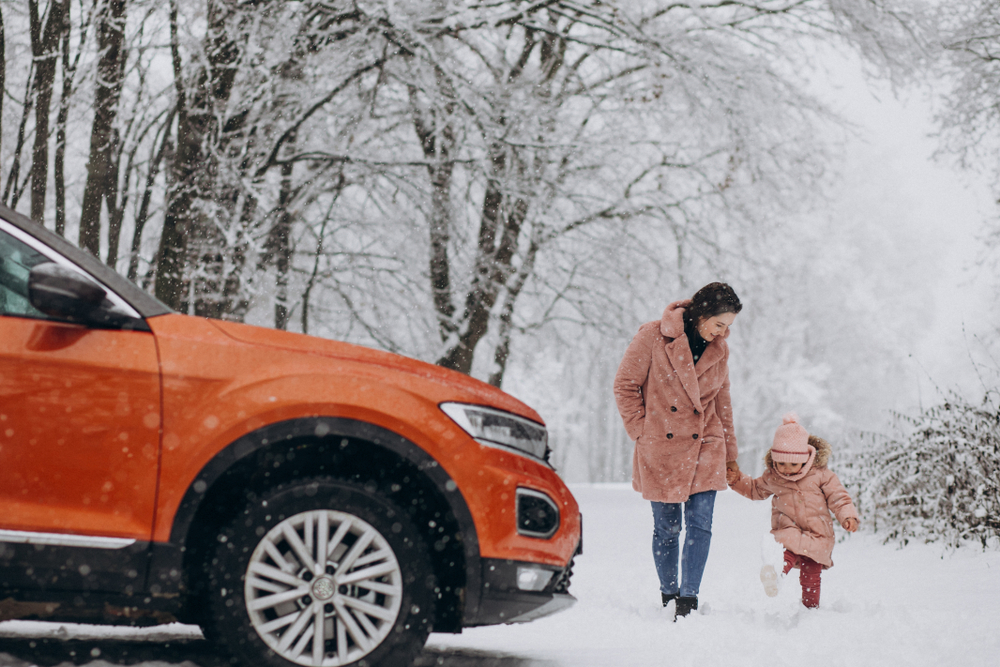 Mother with little daughter in a winter park by car