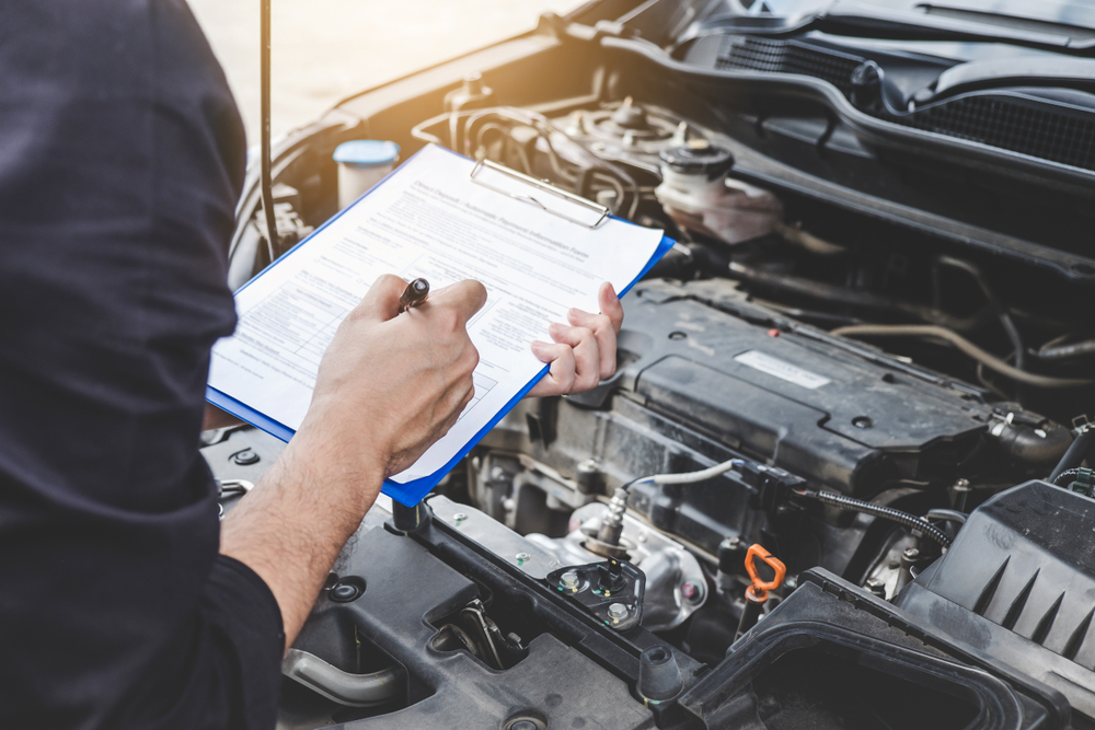 Automobile mechanic repairman checking a car engine with inspecting writing on a clipboard
