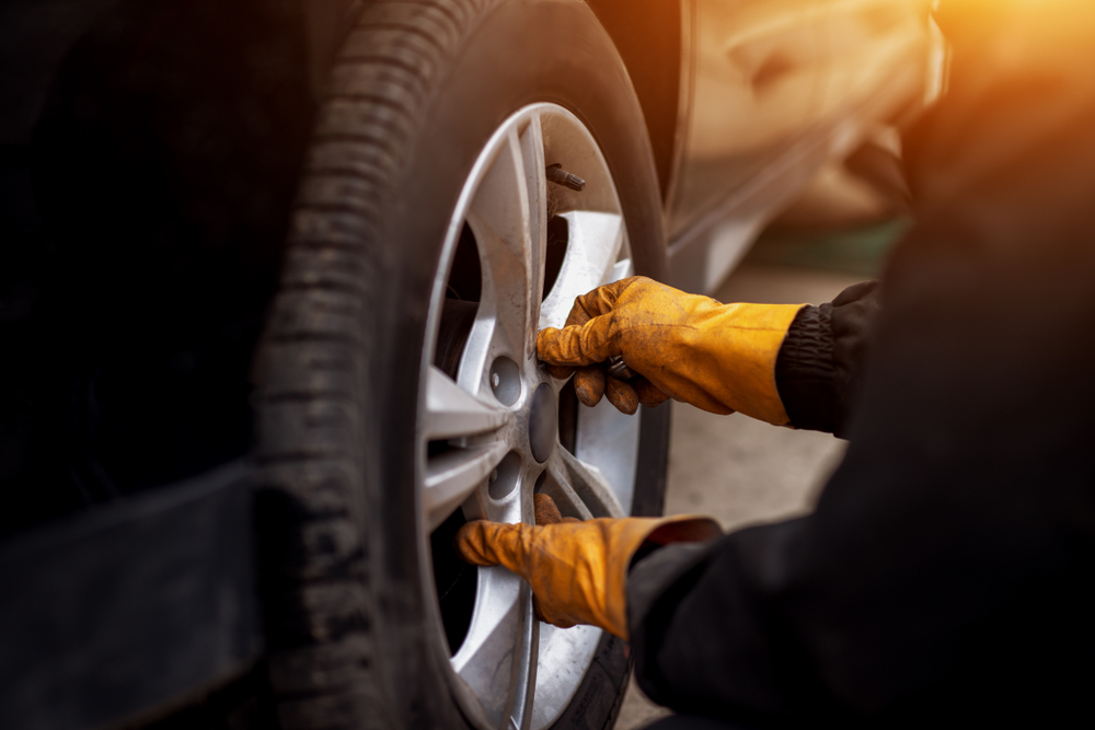 Auto mechanic man with electric screwdriver changing tire outside.