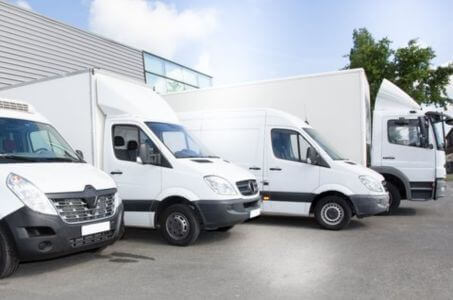 line of commercial delivery vans parked outside a service facility