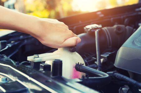 checking the engine coolant reservoir under the hood of a vehicle
