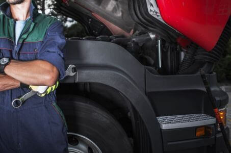 heavy-duty truck technician standing beside an open engine bay during service