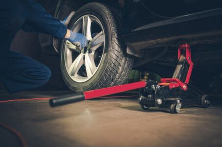 technician removing a car wheel while the vehicle is lifted on a floor jack