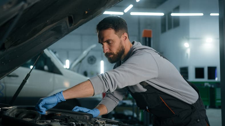 Auto mechanic inspecting and repairing a car engine in a service garage