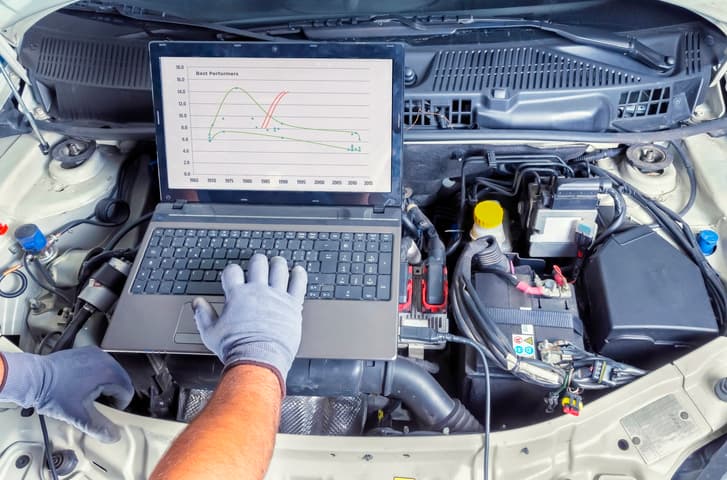 Automotive technician performing computer diagnostics on a car engine