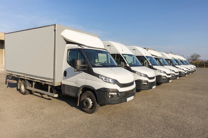 Fleet of white commercial delivery trucks parked in a row outdoors
