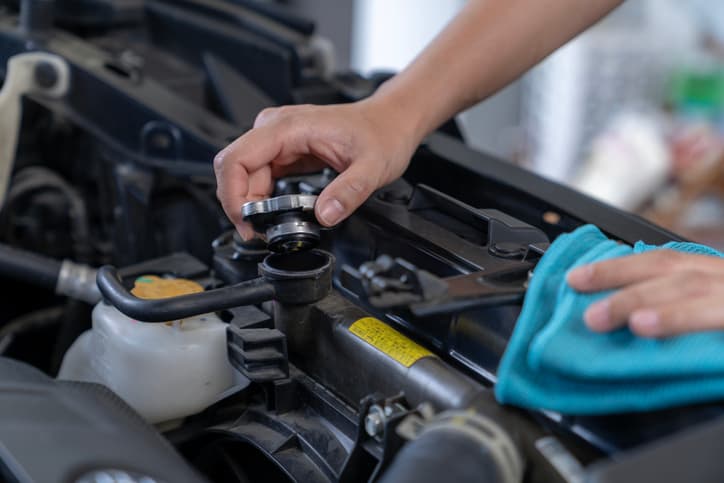 Person removing a radiator cap while inspecting a car cooling system