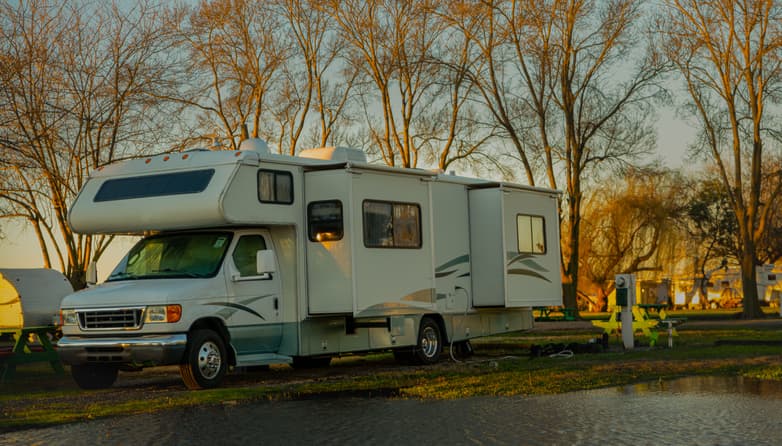 Motorhome RV parked at a campground near a small pond during sunset