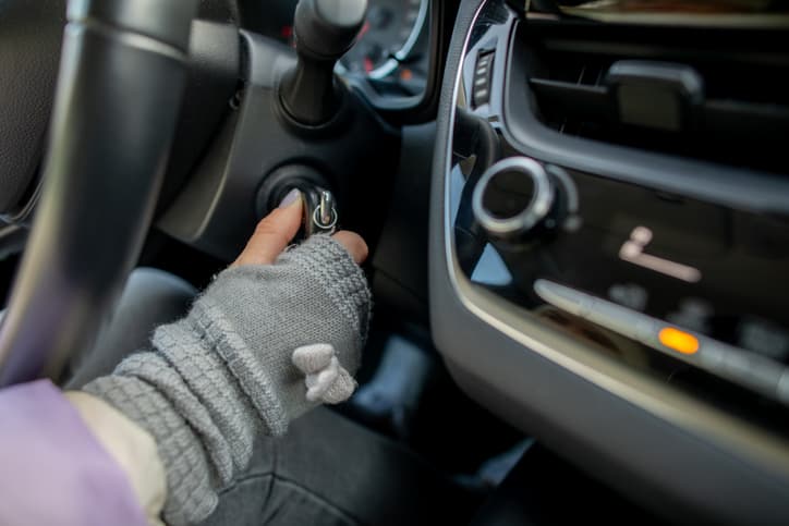 Person starting a car with a key while wearing winter gloves