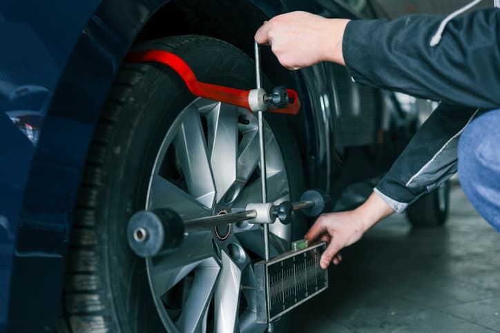 Technician performing wheel alignment on a vehicle tire in an auto shop